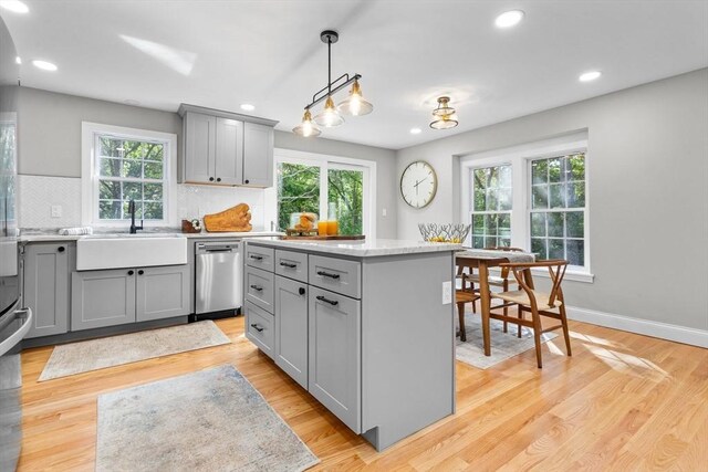 kitchen with sink, tasteful backsplash, a kitchen island, stainless steel dishwasher, and light hardwood / wood-style floors