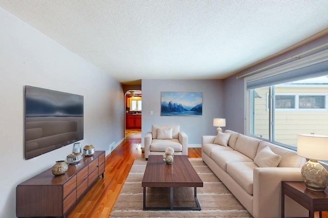 living area featuring a textured ceiling, light wood-type flooring, and baseboards