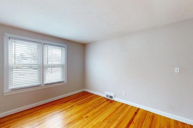 empty room featuring light wood finished floors, baseboards, and visible vents