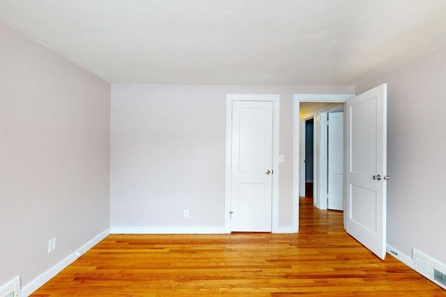 empty room with light wood finished floors, visible vents, and baseboards