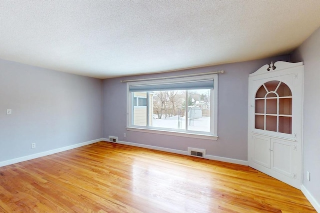 empty room with light wood finished floors, baseboards, and visible vents