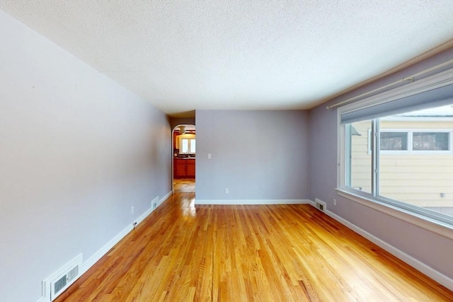 empty room featuring baseboards, visible vents, and light wood finished floors