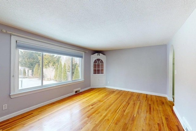 unfurnished room featuring light wood-type flooring, visible vents, a textured ceiling, and baseboards