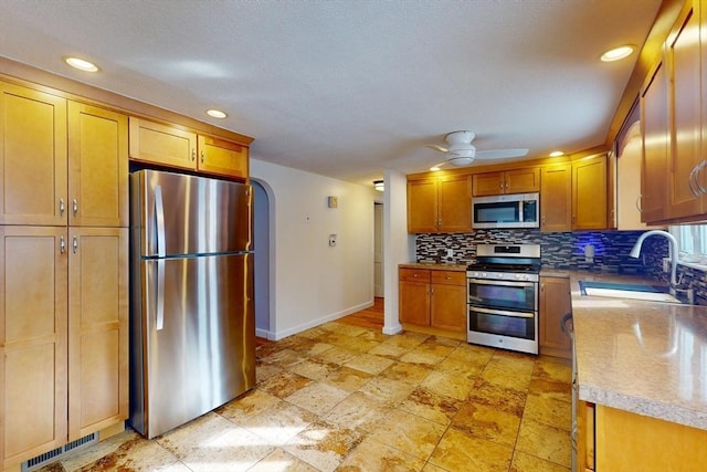 kitchen with arched walkways, tasteful backsplash, appliances with stainless steel finishes, a sink, and baseboards