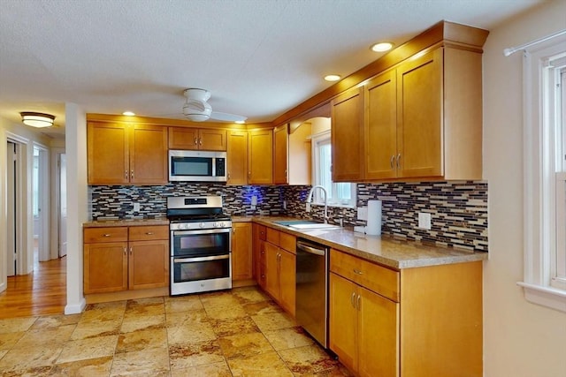 kitchen featuring stainless steel appliances, a sink, backsplash, and a ceiling fan