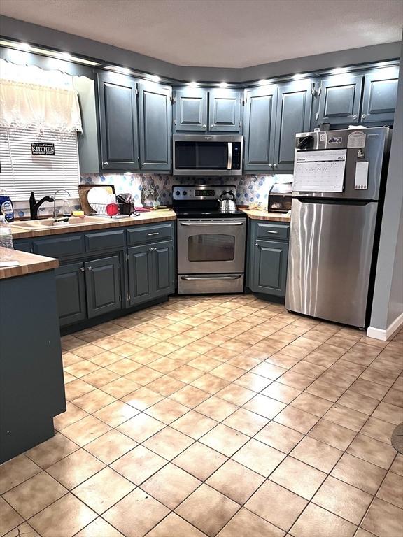 kitchen with tasteful backsplash, sink, light tile patterned floors, and appliances with stainless steel finishes