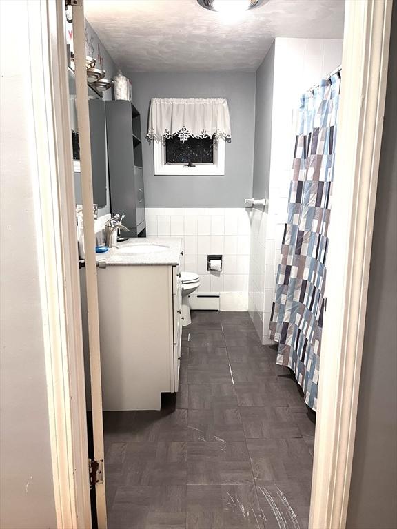 bathroom featuring toilet, a shower with curtain, tile walls, a baseboard radiator, and vanity