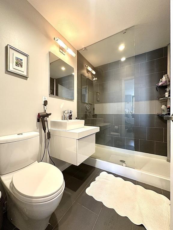 bathroom featuring tile patterned floors, toilet, vanity, and tiled shower