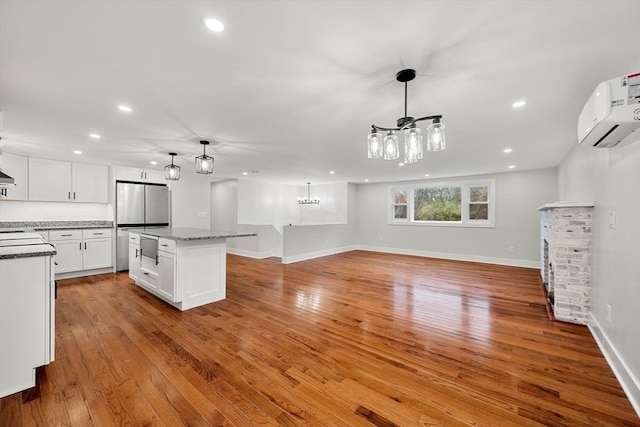 kitchen featuring light stone counters, white cabinetry, light hardwood / wood-style flooring, decorative light fixtures, and a center island