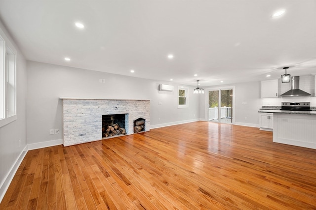 unfurnished living room with a wall unit AC, light hardwood / wood-style flooring, a notable chandelier, and a brick fireplace