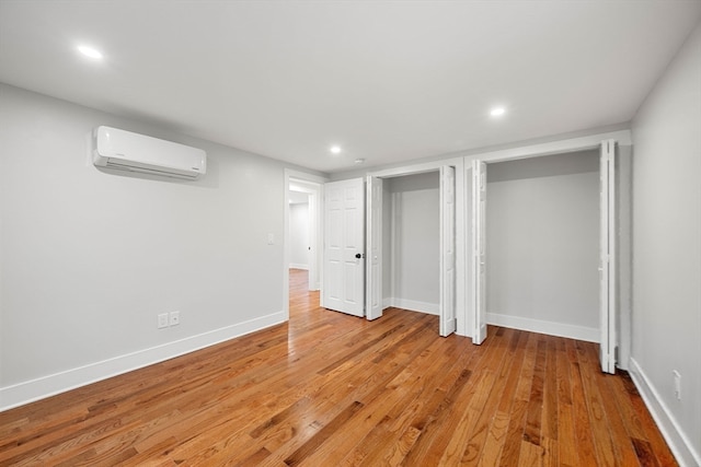 unfurnished bedroom with an AC wall unit and light hardwood / wood-style floors