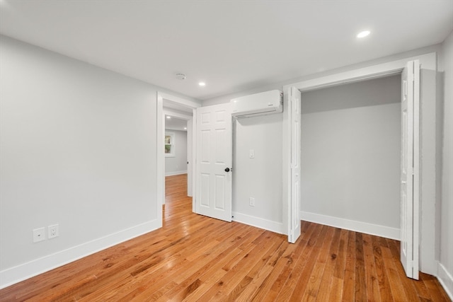 unfurnished bedroom with light hardwood / wood-style flooring, a wall unit AC, and a closet