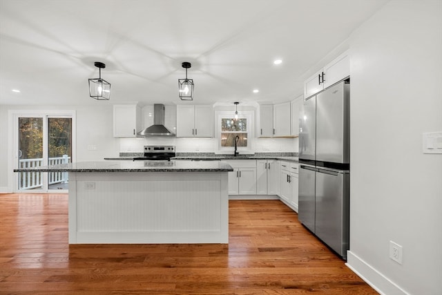 kitchen featuring white cabinets, a kitchen island, appliances with stainless steel finishes, light wood-type flooring, and wall chimney exhaust hood