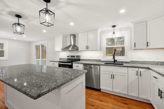 kitchen featuring stainless steel appliances, wall chimney exhaust hood, decorative light fixtures, and white cabinets