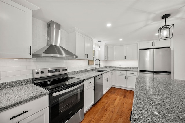 kitchen with sink, appliances with stainless steel finishes, wall chimney range hood, and white cabinets