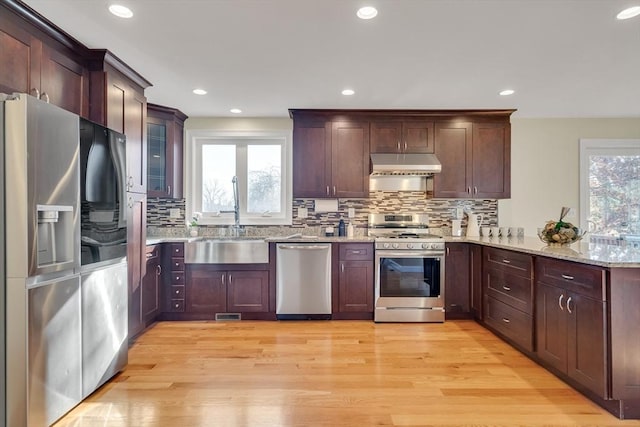 kitchen with sink, appliances with stainless steel finishes, light hardwood / wood-style floors, light stone countertops, and kitchen peninsula