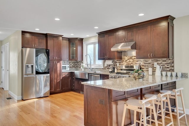 kitchen with appliances with stainless steel finishes, sink, light hardwood / wood-style floors, kitchen peninsula, and light stone countertops