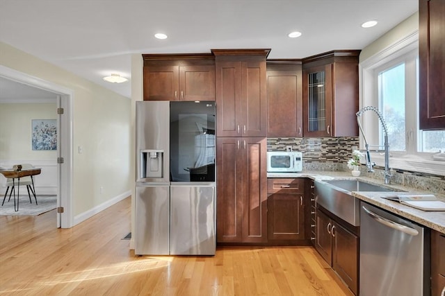 kitchen with appliances with stainless steel finishes, sink, light stone counters, light hardwood / wood-style floors, and crown molding