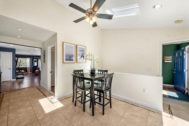 dining room featuring a ceiling fan, tile patterned flooring, baseboards, lofted ceiling with skylight, and recessed lighting