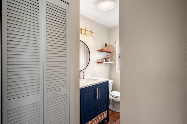 half bath with a closet, wood finished floors, toilet, and vanity