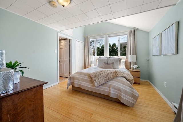 bedroom with baseboards, a baseboard heating unit, and light wood-style flooring