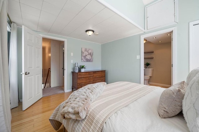 bedroom with baseboards, light wood finished floors, and ensuite bath