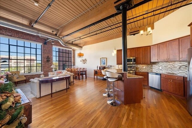 kitchen with appliances with stainless steel finishes, a high ceiling, brown cabinetry, and brick wall