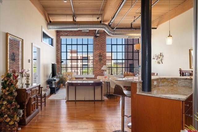 interior space with a towering ceiling, brick wall, wood finished floors, a kitchen bar, and wood ceiling