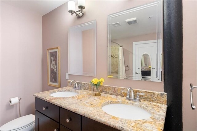 full bath with double vanity, a sink, visible vents, and toilet