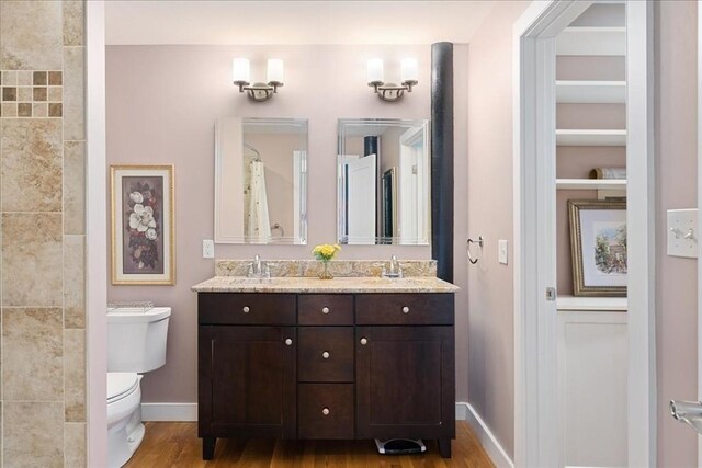 bathroom with double vanity, baseboards, toilet, and wood finished floors