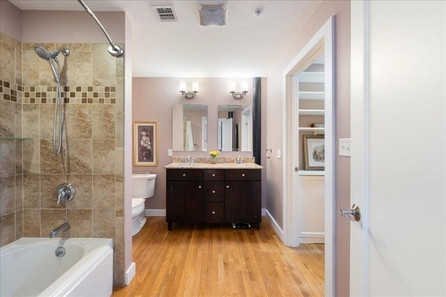 full bath featuring double vanity, bathtub / shower combination, wood finished floors, a sink, and toilet