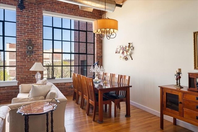 dining space featuring wood finished floors, brick wall, and a healthy amount of sunlight