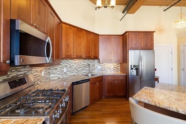 kitchen featuring an inviting chandelier, a sink, stainless steel appliances, wood finished floors, and backsplash