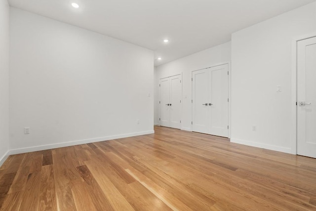 unfurnished bedroom featuring light wood-type flooring, baseboards, two closets, and recessed lighting