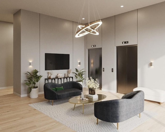 living area featuring a towering ceiling, elevator, light wood-style flooring, and an inviting chandelier