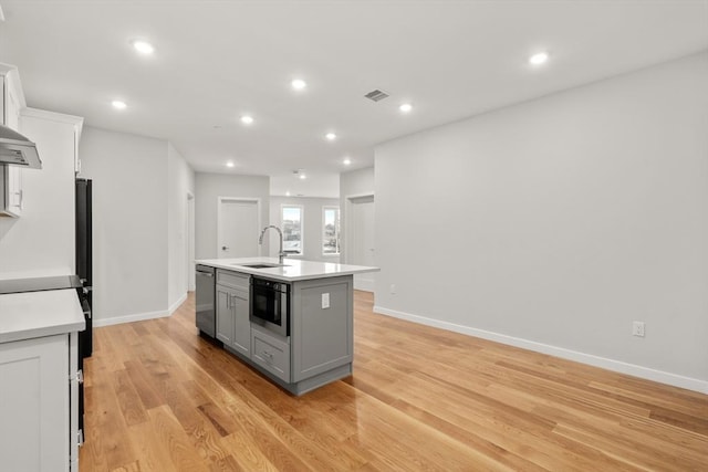 kitchen featuring light countertops, visible vents, white cabinets, a sink, and an island with sink