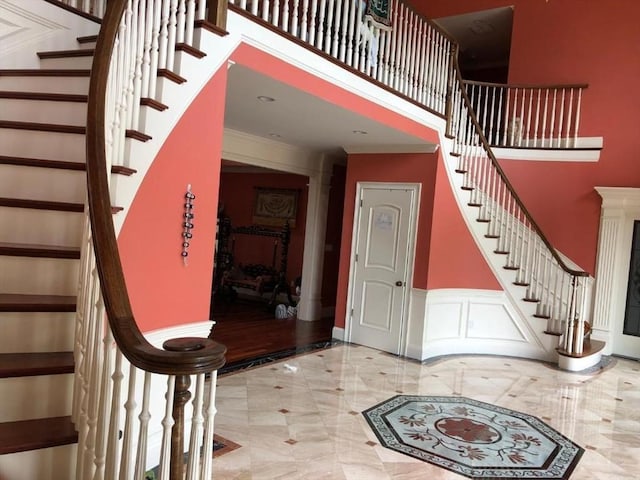 entrance foyer with marble finish floor, a decorative wall, stairway, and a high ceiling