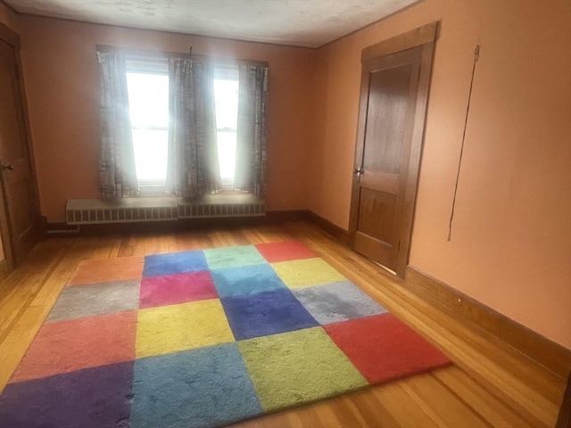 unfurnished room featuring wood-type flooring and a baseboard radiator