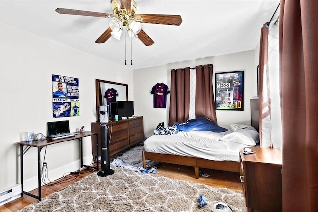 bedroom featuring a baseboard heating unit, ceiling fan, baseboards, and wood finished floors