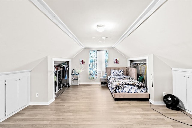 bedroom featuring baseboards, light wood-style flooring, vaulted ceiling, a walk in closet, and a closet