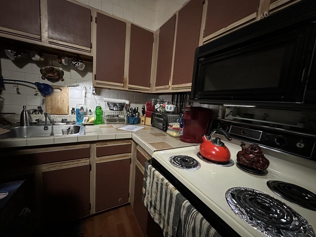 kitchen with range with electric cooktop, a sink, black microwave, backsplash, and tile countertops