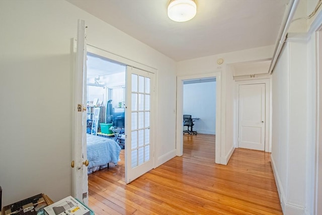 corridor with light wood finished floors, french doors, and baseboards