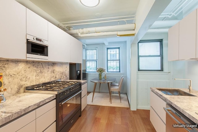 kitchen with gas range, dishwasher, a sink, light wood-type flooring, and tasteful backsplash