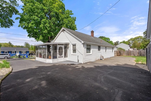 view of home's exterior with a sunroom, fence, and a chimney