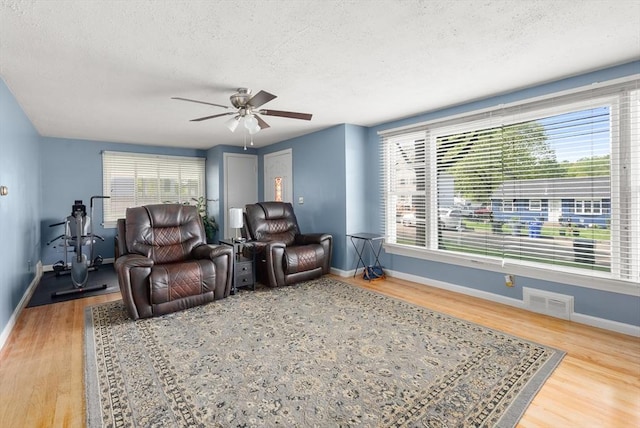 living room with a textured ceiling, baseboards, wood finished floors, and ceiling fan