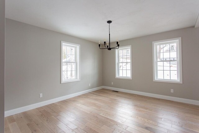 unfurnished room featuring light wood-style flooring, baseboards, and a chandelier