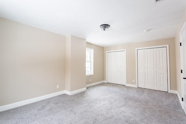 unfurnished bedroom featuring carpet floors, baseboards, and multiple closets