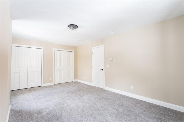 unfurnished bedroom with carpet, baseboards, and two closets