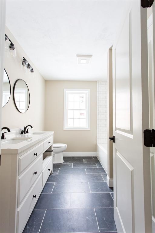 full bath with a tub to relax in, vanity, toilet, and baseboards