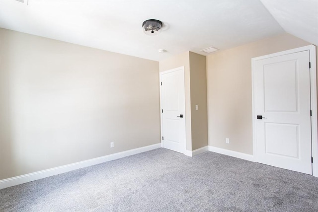 carpeted spare room featuring baseboards and vaulted ceiling